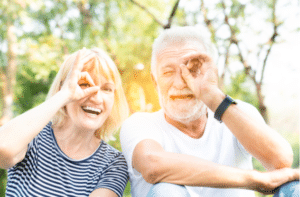 Seniors in the park with happy face smiling doing ok sign with hand on eye looking through fingers.