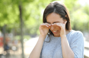 Woman rubbing her eyes standing outdoors in a park