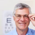 A happy patient showing off his new spectacles while standing in an optometrist's office