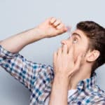 side view portrait of handsome man in checkered shirt applying eye drop over grey background