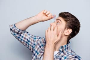 side view portrait of handsome man in checkered shirt applying eye drop over grey background